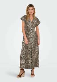 Robe maxi imprimée léopard en beige et marron, avec des manches courtes, un décolleté en V et une fermeture à boutons sur le devant. Portée avec des sandales à talons compensés.