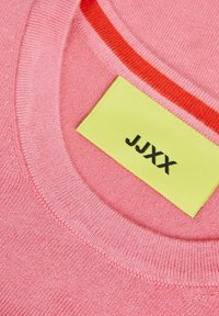 Maglione rosa con colletto a girocollo a coste, caratterizzato da una striscia rossa. L'etichetta è gialla con testo nero "JJXX." Morbida texture, tessuto lavorato a maglia.