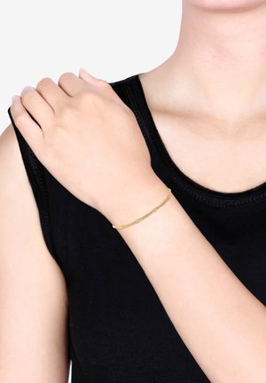 Gold-tone bracelet with a textured surface, featuring a delicate, slim design. Worn on a wrist, contrasting against a black top.