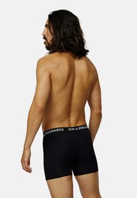 Boxer shorts en coton noir avec une ceinture élastique de marque, offrant un ajustement serré et une texture lisse. Vue de l'arrière.
