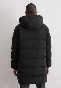 Schwarze Pufferjacke mit abnehmbarem Kapuzen, horizontalen Nähten, einer gesteppten Textur und einem mittellangen Design.