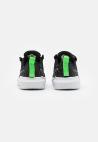 Black sneakers with a textured fabric upper, white speckled soles, and bright green pull tabs on the heels. Rubber accents near the sole.