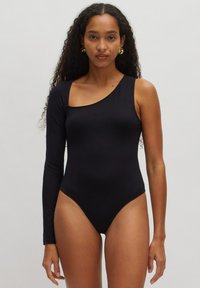 Zwarte badpak met asymmetrisch ontwerp; heeft één lange mouw en één schouderuitsnijding. Gladde, rekbare stof; minimalistische stijl.
