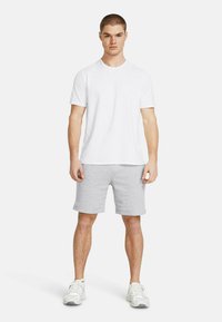Vit t-shirt med kort ärm i kombination med grå shorts. T-shirten har en rund halsringning och en slät textur. Shortsen har ett elastiskt midjeband.