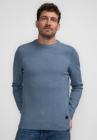 Pulover albastru deschis, realizat dintr-un material moale, având guler rotund, manșete cu bandă și detalii laterale. Croială clasică cu un etichetă la baza puloverului.