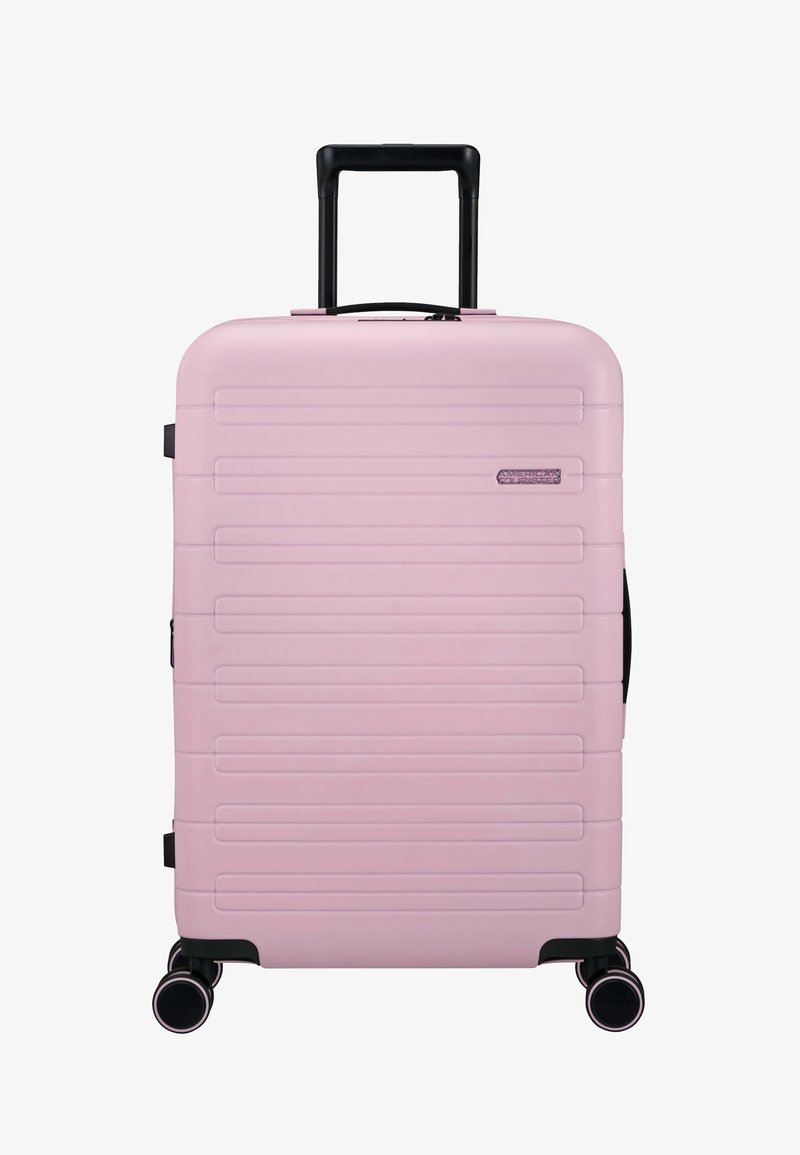 Valise rigide rose avec des rainures horizontales, accents noirs, poignée télescopique et quatre roues multidirectionnelles pour un transport facile.