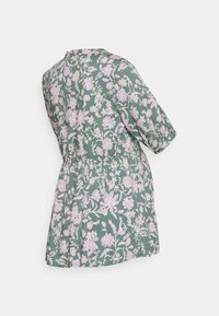 Camisa com padrão floral em tecido verde com flores rosa claras. Mangas curtas, cintura ajustada e bainha curvada, exibindo um corte descontraído.
