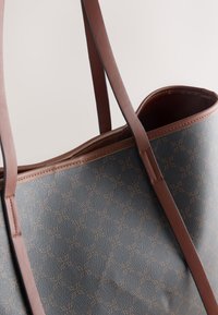Sac fourre-tout bleu avec une surface texturée, doté de bretelles marron et d'un motif géométrique embossé. Conception à ouverture supérieure avec un intérieur lisse.