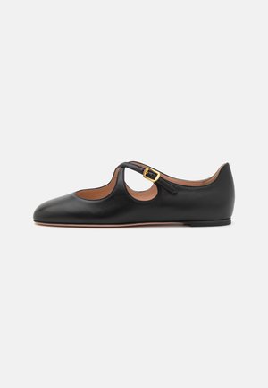 Zapato plano de cuero negro con diseño de corte, tira de tobillo y detalle de hebilla dorada. Textura suave con punta redondeada y tacón bajo.
