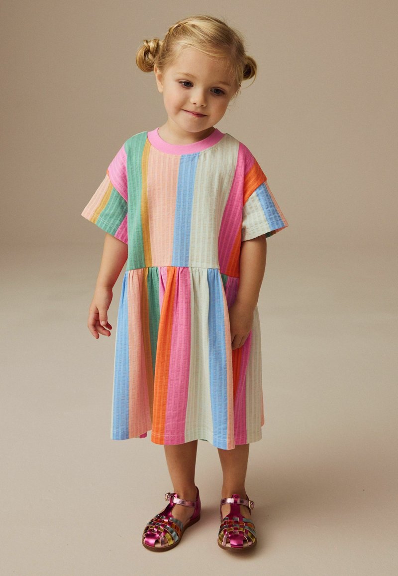 Kleurvolle gestreepte jurk met korte mouwen, inclusief roze, groen, oranje en blauwe tinten. Gepaarde met metallic roze sandalen.