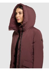 Bordó színű steppelt kabát nagy, bélelt kapucnival, elöl cipzárral, patentgombokkal és oldalzsebekkel; sima, matt felület.