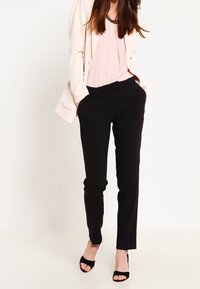 Pantalones negros ajustados con corte slim, combinados con una blusa rosa claro y un blazer crema. Tejido suave y diseño minimalista.