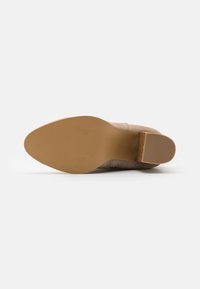 Lichtbeige hoge hak schoen met een ronde neus, zacht suede materiaal en een gladde rubberen zool met een gestructureerd patroon en een bescheiden hak.