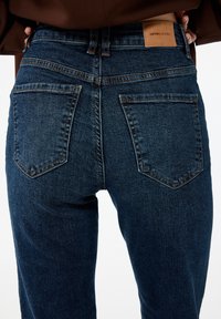 Jeans in denim blu scuro con vita aderente, due tasche posteriori e un’etichetta in pelle sul retro. Presenti dettagli di cucitura.