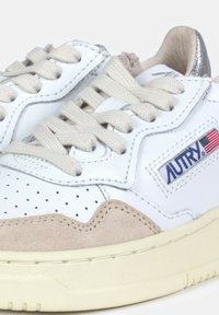 Sneaker bianche in pelle con accenti in suede beige, dettagli perforati, lacci beige e una linguetta sul tallone argentata. Presentano un'etichetta "AUTRY".