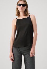 Camisole nera in satin con spalline sottili, caratterizzata da un scollo quadrato e una texture liscia, abbinata a pantaloni larghi grigi con una texture a righe.