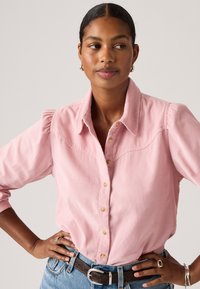 Chemise en velours côtelé rose clair avec un devant boutonné, des manches courtes bouffantes et un design de patte courbée, associée à un jean en denim taille haute.