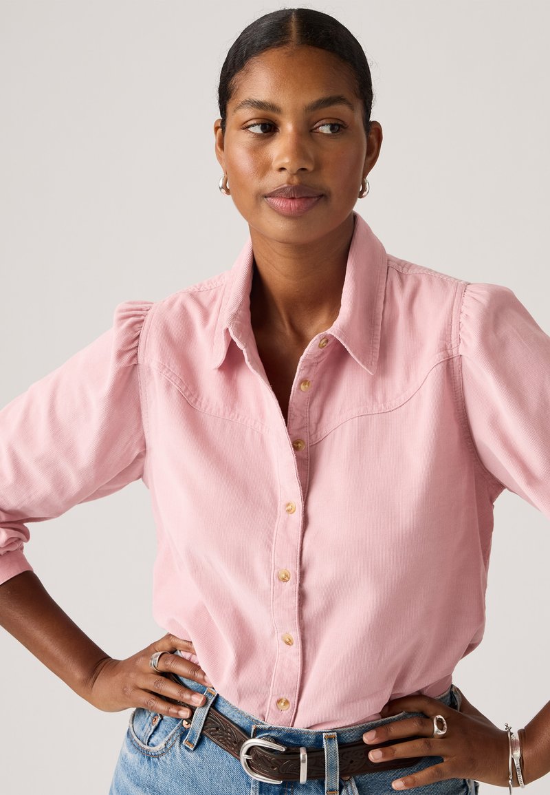 Chemise en velours côtelé rose clair avec un devant boutonné, des manches courtes bouffantes et un design de patte courbée, associée à un jean en denim taille haute.