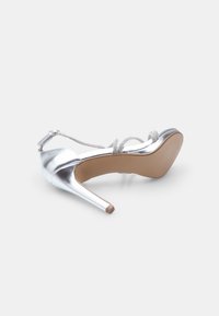 Strieborné sandále na vysokom podpätku s lesklým povrchom, trblietavé remienky na členku a štíhle stiletto podpätky. Béžová gumená podrážka.