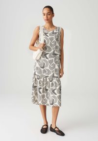 Sleeveless dress with a black and white wavy line pattern, tiered hem, made of lightweight fabric. Paired with black mesh shoes and a small handbag.