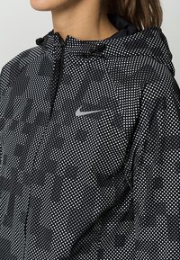 Veste à capuche à motif noir et blanc, dotée d'une fermeture éclair et d'un petit logo Nike argenté sur la poitrine. Tissu léger.