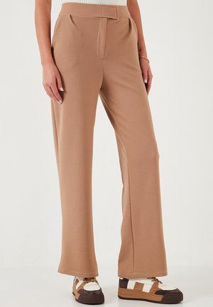 Beige wide-leg trousers with a textured fabric. Features a flat front with a subtle crease and a fitted waist. Accented with sporty shoes.