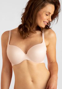 Lichtroze gewatteerde beha met verstelbare bandjes, naadloze cups en een zachte textuur, ontworpen voor comfort en ondersteuning.