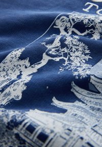 White architectural and tree illustration printed on textured blue fabric with partial visible text at the top.