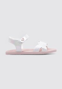Sandalias blancas con correa ajustable, que presentan un diseño de ala recortada. Suela plana rosa, textura suave con sutiles perforaciones, estilo casual.