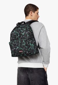 Mochila negra con un patrón similar al agua en verde y púrpura, hecha de un tejido duradero, que cuenta con un bolsillo frontal y tirantes ajustables.