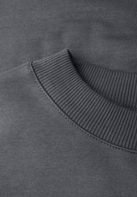 Szary materiał bluzy z ribbowanym dekoltem typu crew. Tekstura jest gładka i jednolita, z minimalnie widocznymi szwami przy kołnierzu.