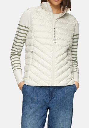 Gepolsterte Weste in hellem Beige mit Reißverschluss vorne und Zickzack-Steppung. Über einem gestreiften, langärmeligen Oberteil in Grün und Weiß getragen. Lässige Passform.