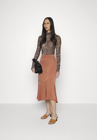 Camisola de manga longa com padrão de leopardo, saia cor ferrugem com bainha rodada, bolsa preta com acessórios franzidos, sandálias de salto cor bege.