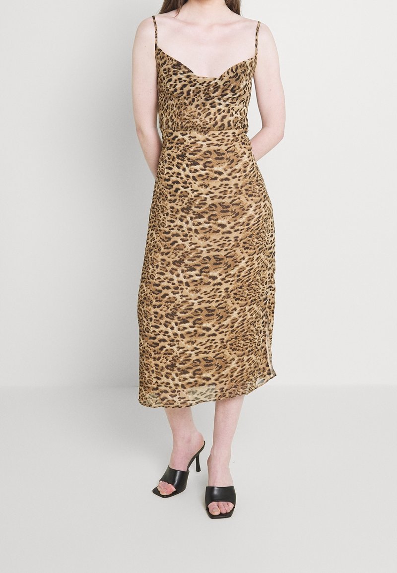 Robe midi à imprimé léopard avec fines bretelles spaghetti, tissu lisse et silhouette cintrée. Associée à des mules à talons ouvertes noires.