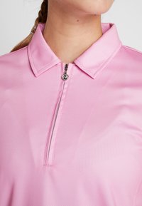 Vaaleanpunainen poolopaita, jossa on vetoketjupanta ja teksturoitu kangas. Sisältää hopeiset vetoketjuvarusteet ja rakenteellisen kaulussuunnittelun.