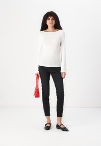 White long-sleeve top, black slim-fit jeans, black flats with metal accents, holding a red handbag. Simple lines and contrasting colors.