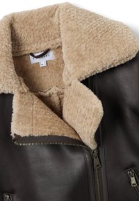 Giacca in pelle marrone con colletto in eco shearling beige. Presenta due zip e una finitura liscia sul corpo. Etichetta visibile all'interno.