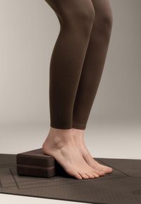 Joogablokk, mis on valmistatud tumedast vahtmaterjalist, ristküliku kujuline ja ümarate servadega, asetatud tekstuursele hallile mattile. Paljad jalad resting blokil.