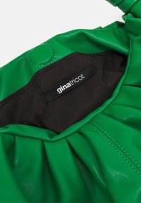 Grön faux läderväska med samlad design, som har ett svart inre, synliga sömmar och en etikett med texten "ginatricot."