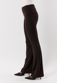 Pantaloni marroni a vita alta con gambe svasate, realizzati in un tessuto liscio e elastico. Presentano una cerniera sul retro e una vestibilità sartoriale.