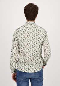 Camicia bianca con motivo floreale verde, maniche lunghe e colletto. Abbinata a jeans blu, mostra una vista casual da dietro.