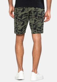 Pantaloni cargo da uomo in misto cotone verde e nero, con taglio rilassato, lunghezza al ginocchio e vita a costine. Indossati con sneaker bianche.