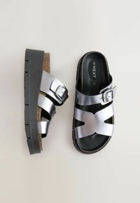 Sandali infradito metallici argento con soletta in sughero, fibbia regolabile e suola nera testurizzata. Presentano cinturini incrociati per un migliore supporto.