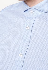 Camicia button-up azzurro chiaro con un motivo herringbone testurizzato, colletto classico e bottoni trasparenti a quattro fori.