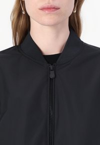 Black bomber jacket with a zippered front, ribbed collar, and smooth texture; features a minimalist design with no visible patterns or accents.