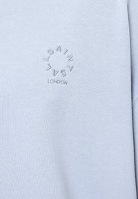 Lichtblauwe sweatshirt met een zachte textuur en geborduurd cirkelvormig logo met de tekst "SAINT LAURENT LONDON" in grijs op de voorkant.