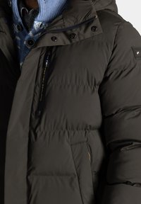 Donker olijfgroene pufferjack met een glanzende afwerking, voorzien van een afneembare capuchon, ritssluiting en meerdere zakken. Accenten omvatten een logopatch.