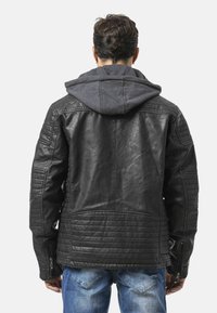 Schwarze Leder-Motorradjacke mit gesteppten Details an Schultern und Rücken, darunter ein grauer Hoodie, Rückansicht.