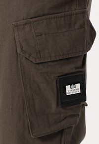 Brown cargo pants with a textured fabric, featuring large side pockets and a black rectangular label reading "WEEKEND OFFENDER."