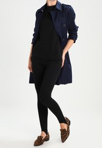 Marinblå trenchcoat med en slät textur, svart överdel, svarta leggings och skor med leopardmönster, med en skräddarsydd passform och synliga knappar.
